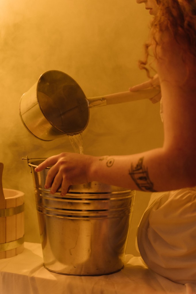 Photo is of a person pouring a pan of water into a silver bucket.